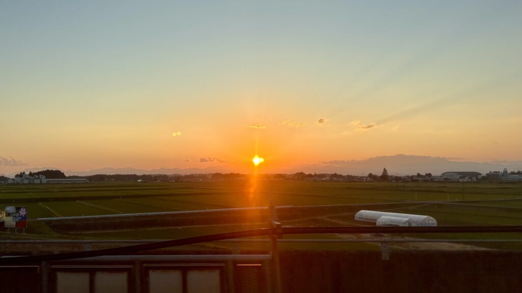 走る新幹線やまびこの車窓から眺める、地平線に沈んでいく美しい夕日とオレンジ色の空